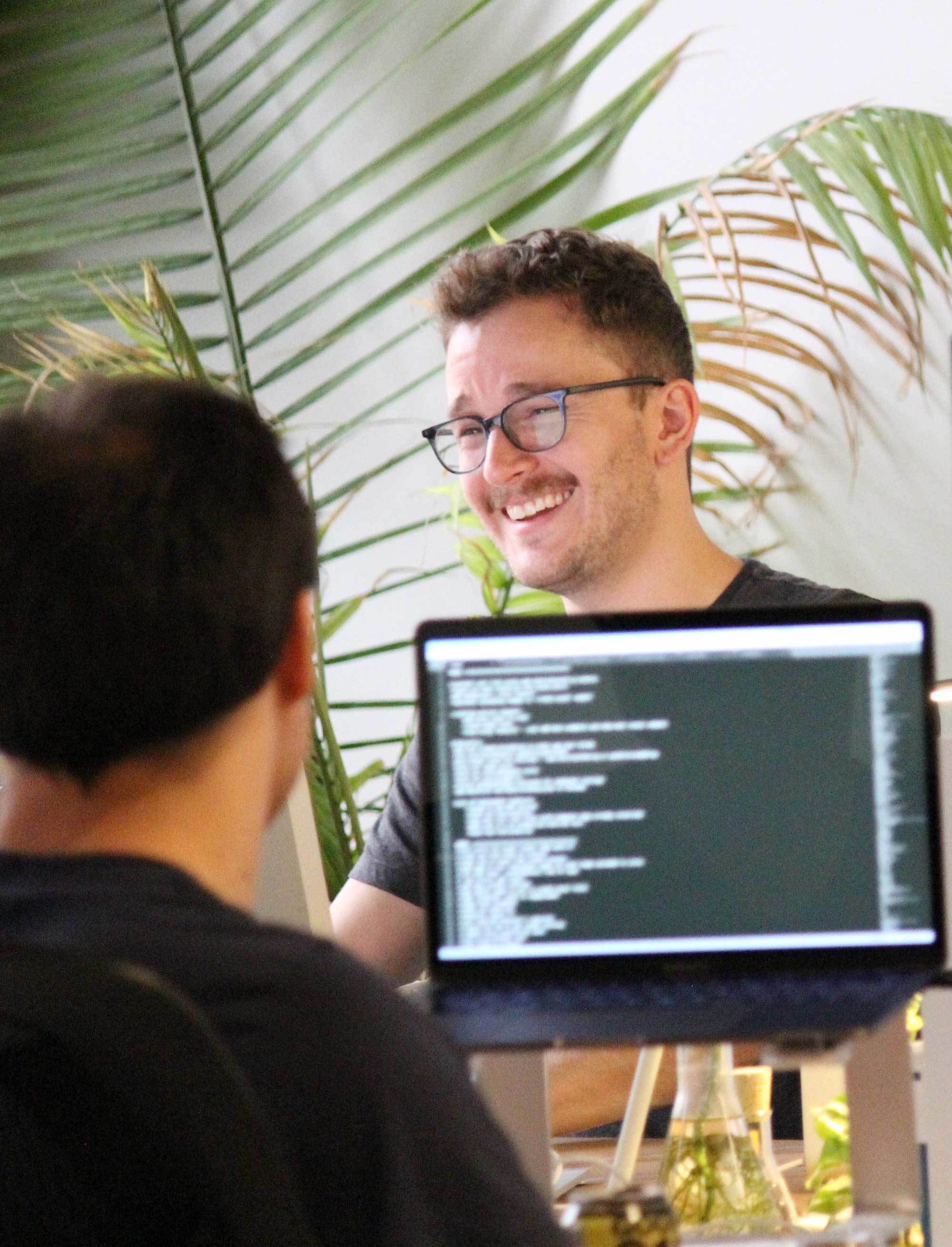 Photo of a Crema employee coding and another behind him smiling